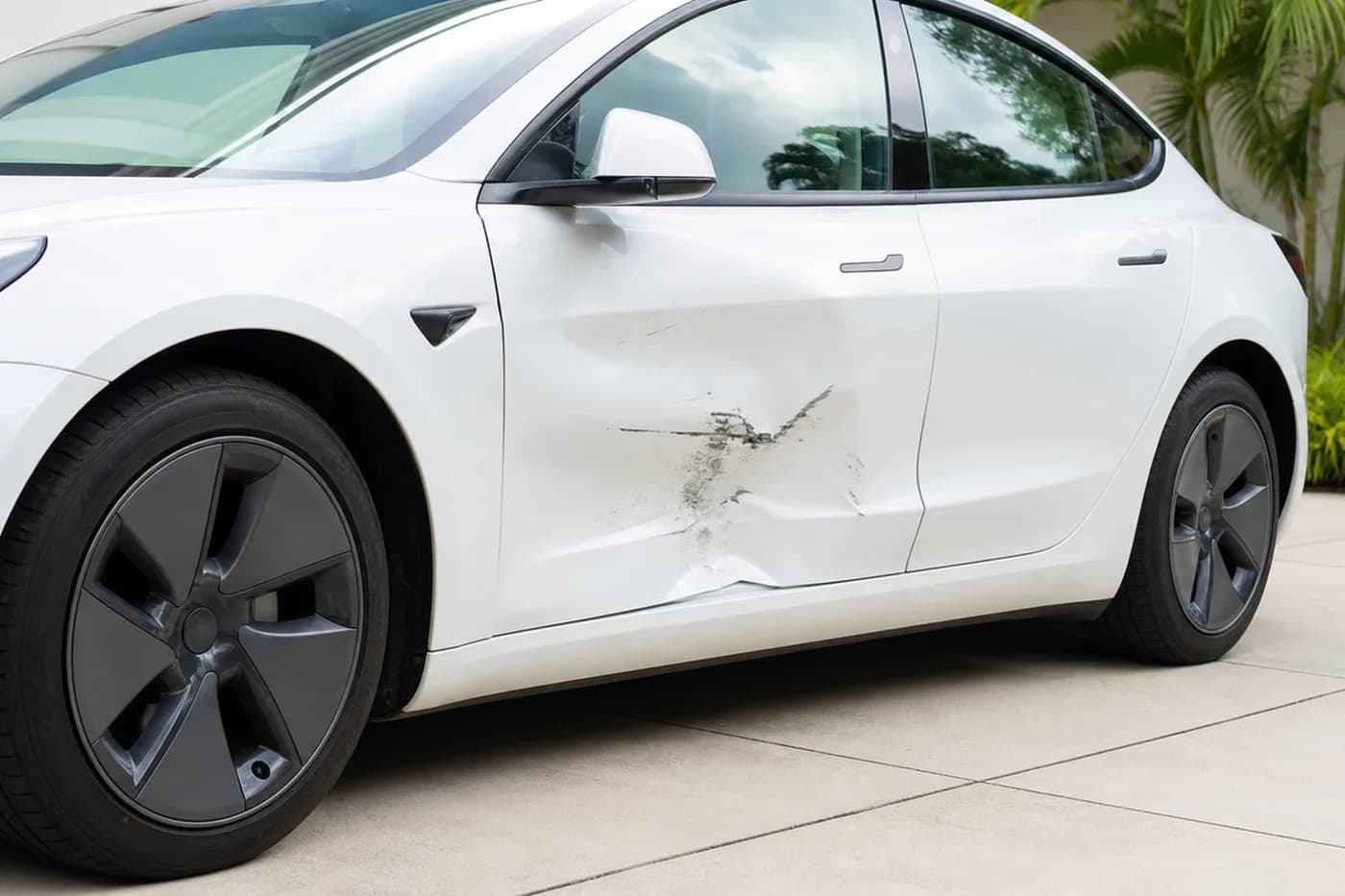 White electric sedan with a dent and scraped paint on the left front door